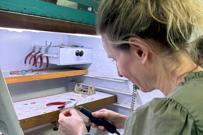 Caron Bluestone in a green blouse at a jewellery workbench with a powered handpiece and red-handled pliers