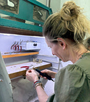 Caron Bluestone in a green blouse at a jewellery workbench with a powered handpiece and red-handled pliers
