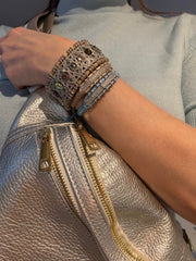 Woman wearing a layered stack of sand and blue thread natural diamond bracelets beside a metallic handbag