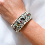 Close-up of a wrist wearing a decorative bracelet with diamonds and gemstones on a white background