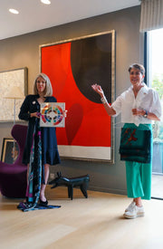 Two women standing in a room with a large abstract painting in the background