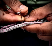 Close-up of hands threading a needle with a pink and silver bespoke diamond bracelet.