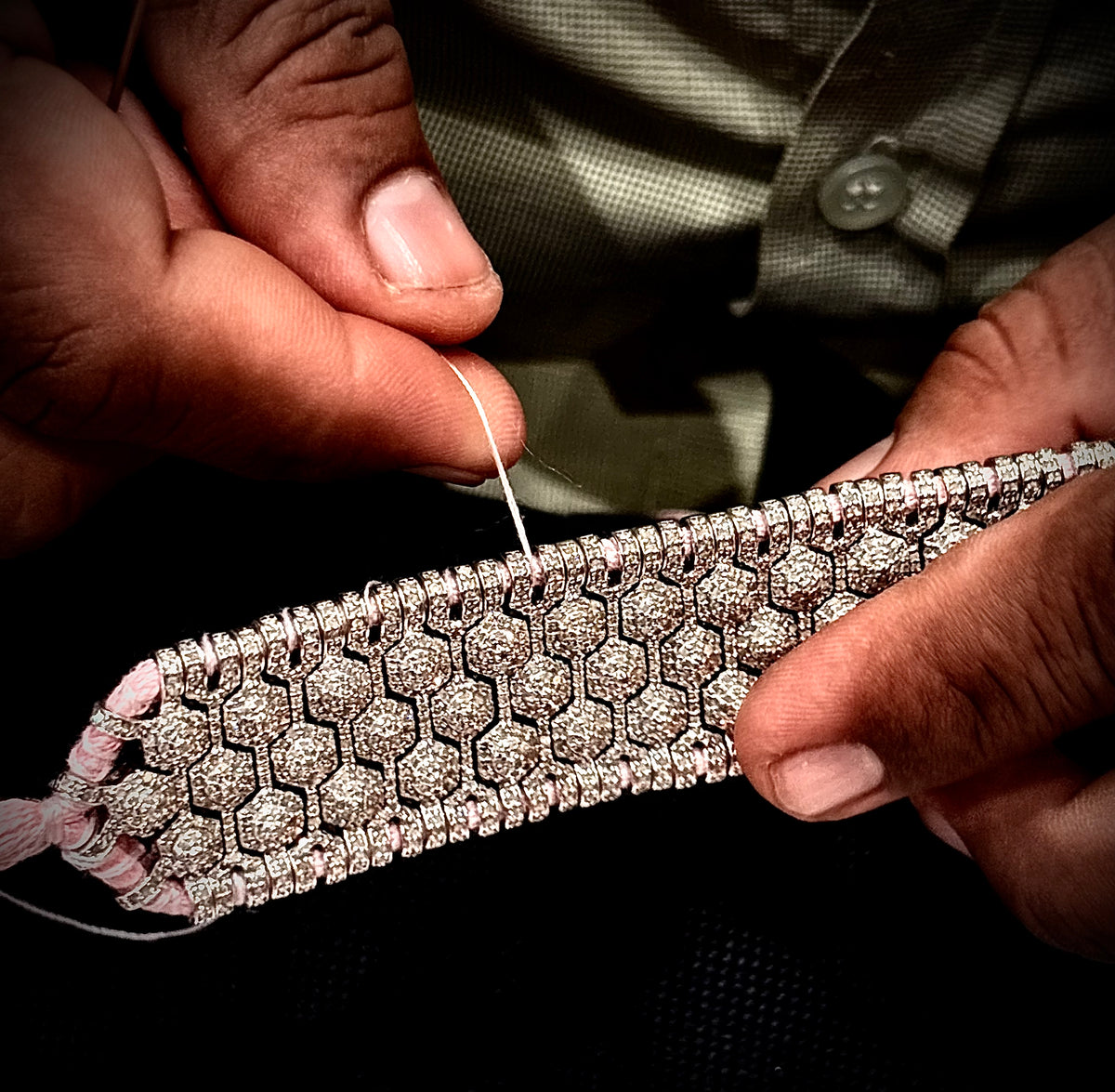 Artisan holding a wide pavé diamond bracelet while stitching pink thread