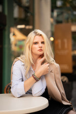 Woman sitting at a table outdoors with a blurred background. She wears 3 of the Mini Collection, diamond and gemstone bespoke bracelets by Caravan  of Stones. 