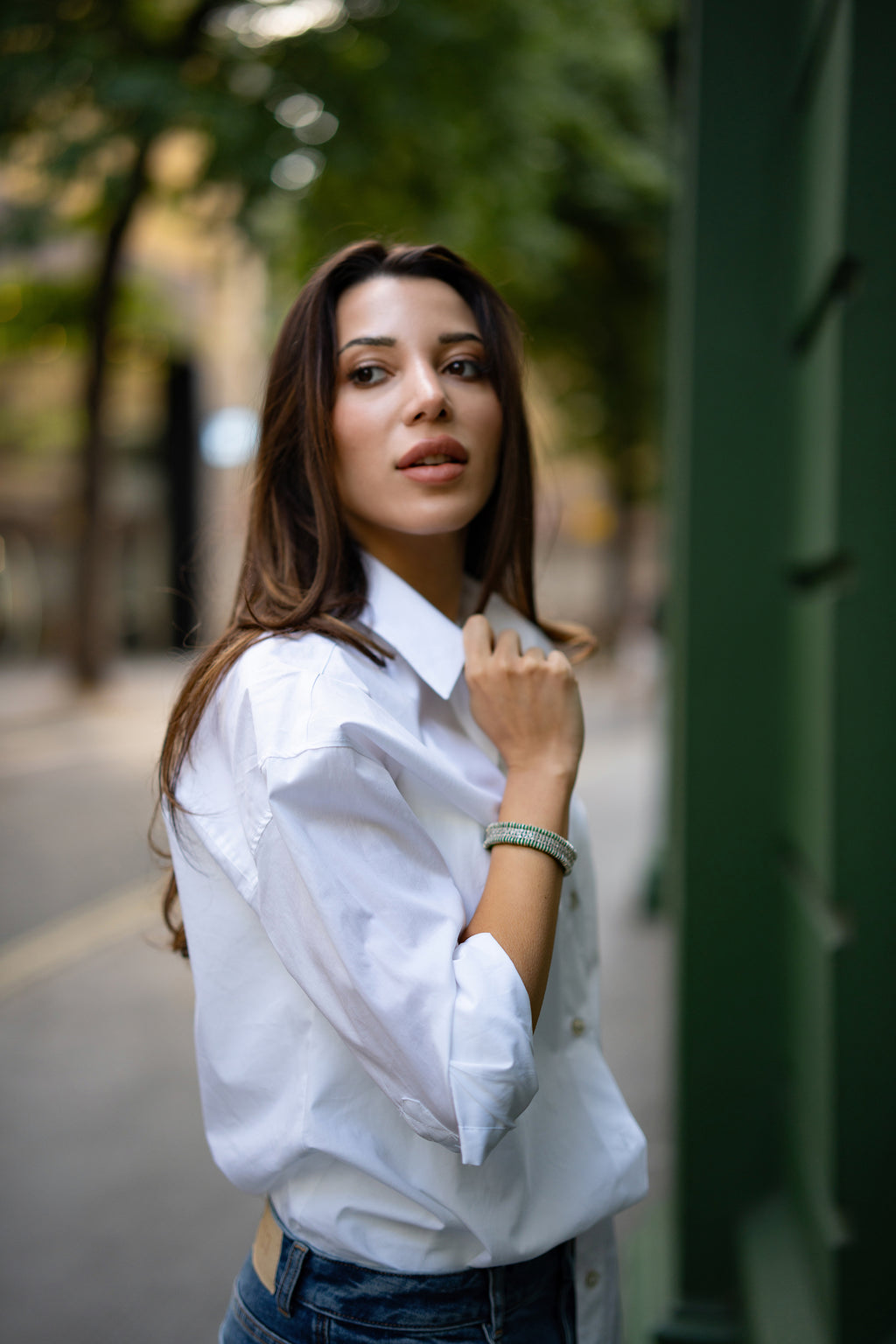 Woman wearing a white shirt and blue jeans, she shows her bespoke diamond thread bracelet by Caravan of stones and is standing outdoors with blurred background