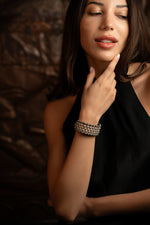 Woman wearing a bespoke Caravan of Stone's diamond bracelet, pointing to her neck against a dark background