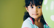 Child holding a green balloon against a green background