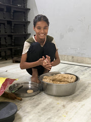 Person smiling beside a bowl of dough in a community kitchen